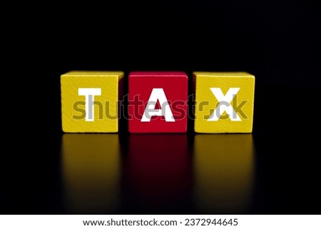 The word "TAX" on coloured wooden block on black surface. Financial and economy concept