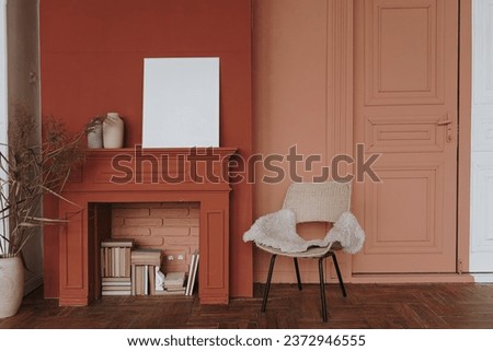 Elegant Scandinavian hygge style home living room interior. Cozy chair, fireplace, blank picture frame, red walls. Aesthetic luxury bright apartment interior design concept