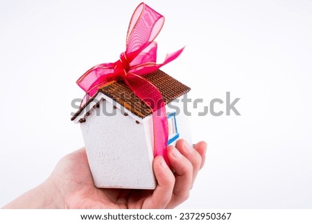 Hand holding a model house with a pink ribbon