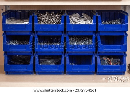 Blue box with small construction objects. Many storage compartments are filled with construction supplies containing screws, nuts, bolts, nails and other workshop tools. Royalty-Free Stock Photo #2372954161