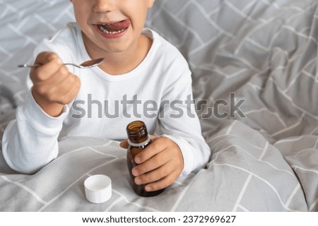 Cute happy toddler child holding in hands spoon with natural cough syrup. Health medicine concept. Cough syrup in bottle. Pediatrician prescription for a child. Royalty-Free Stock Photo #2372969627