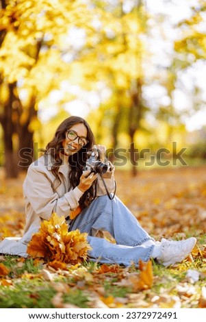 Happy young woman in stylish clothes takes pictures with a retro camera, having fun and relaxing in the autumn sunny park. The concept of relaxation, leisure activities.