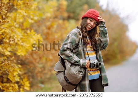 Woman tourist with a retro camera and backpack on a hike in a yellow autumn forest. Young woman walking and having fun outdoors.