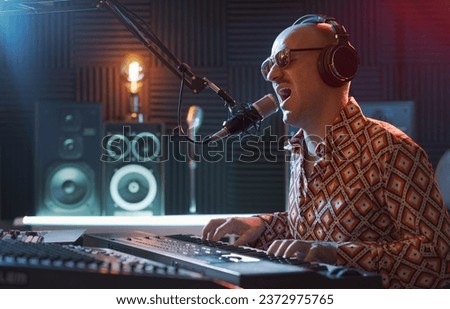 Cool fashionable artist working in the recording studio, he is singing and playing the keyboard
