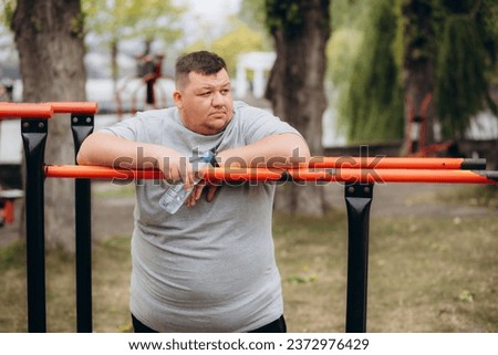 Picture of fat man looks tired while drinking a bottle of water after exercising in the park. High quality photo