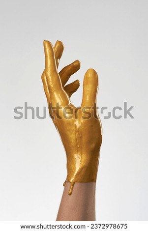 The hand is in gold acrylic paint, the paint covers the hand like a latex glove on light background.