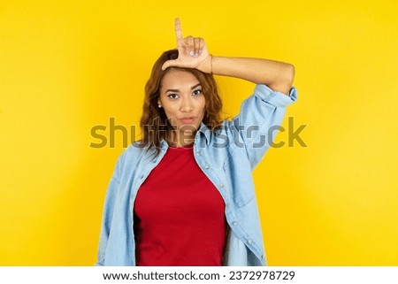 Young beautiful woman making fun of people with fingers on forehead doing loser gesture mocking and insulting.
