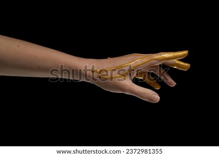 Female hand in liquid gold on a black background.