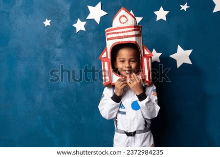 African-American boy in an astronaut costume stands against a background of a blue wall with a starry sky