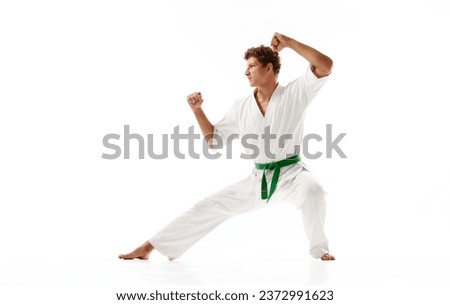 Young guy, karate sportsman in white kimono and green belt standing in pose to fight isolated on white studio background. Concept of martial arts, combat sport, energy, strength, health. Ad Royalty-Free Stock Photo #2372991623