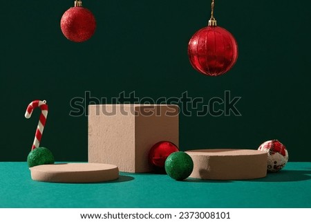 Podiums in square and round shaped are decorated over green background. Red baubles hanging above. Christmas, Christian festival celebrating the birth of Jesus Royalty-Free Stock Photo #2373008101