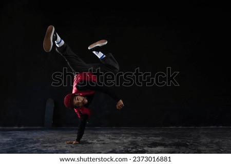 Full body of young Asian man hip hop dancer wears red jacket clothes and tattoos on his body playing and dancing breakdance with posing show on stage in dark background studio. Hip hop dance concept.