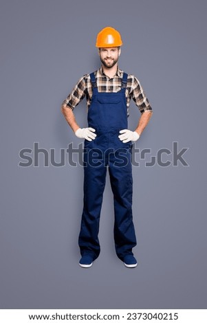 Full size fullbody portrait of joyful attractive repairer in shirt and overall, holding his arms on waist, looking at camera, isolated on grey background Royalty-Free Stock Photo #2373040215