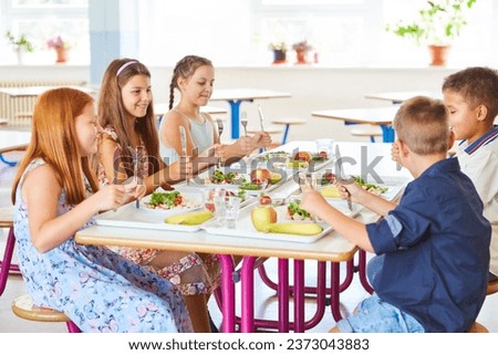 Smiling school children holding cutlery while sitting at table during lunch break in canteen Royalty-Free Stock Photo #2373043883