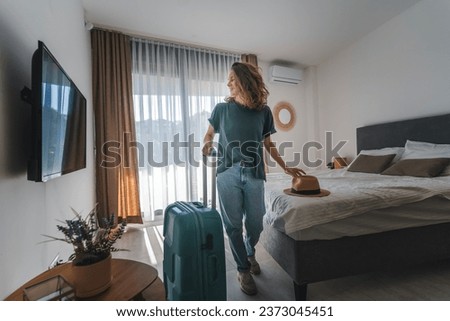 A young woman in a hat with a suitcase checks into a hotel room. Booking and Accommodation travel  Royalty-Free Stock Photo #2373045451