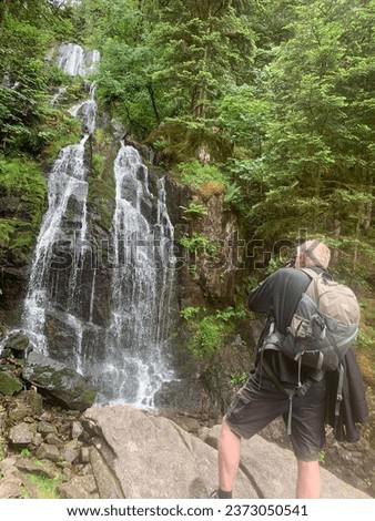 Tourist making pictures of the Grande Cascade de Tendo a beautiful waterfall landscape in the middle of the Vosges forest