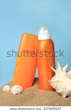 Sand with bottles of sunscreens and seashells against light blue background. Sun protection