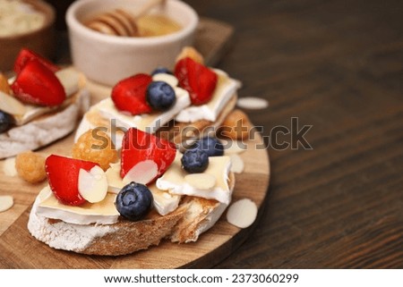 Tasty sandwiches with brie cheese, fresh berries and almond flakes on wooden table, closeup. Space for text Royalty-Free Stock Photo #2373060299