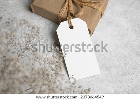 Gift box with blank tag and dried flowers on grey background, white tag card with copy space