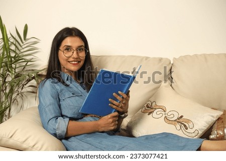 Pretty Young woman sitting on cozy couch sofa and relaxing in her living room reading book in Lifestyle Concept