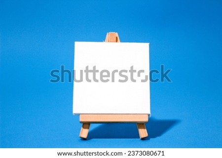 Horizontal photograph of a blank white canvas on an easel with copy space and isolated on blue background 