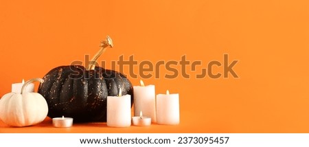 Painted pumpkins and candles on orange background with space for text. Halloween celebration