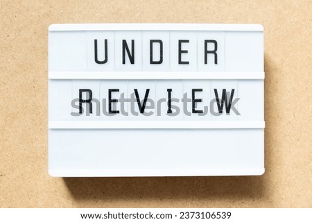 Lightbox with word under review on wood background Royalty-Free Stock Photo #2373106539