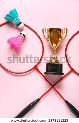 Gold cup with badminton rackets and shuttlecocks on pink background