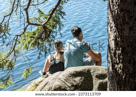 A young couple sits on a stone by a lake and replenishes their energy with food before the next hike in the mountains