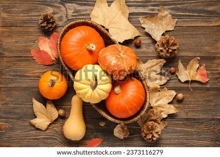 Wicker bowl with fresh pumpkins and autumn leaves on wooden background