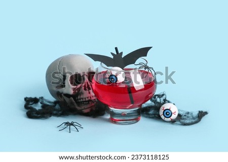 Glass of delicious cocktail, skull and eyes for Halloween celebration on blue background