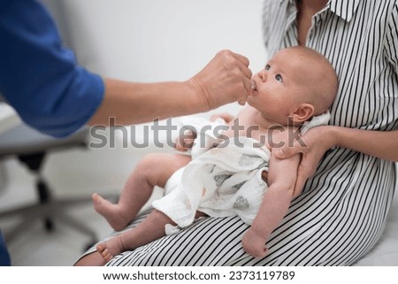 Pediatrician administring oral vaccination against rotavirus infection to little baby in presence of his mother. Children health care and disease prevention. Royalty-Free Stock Photo #2373119789