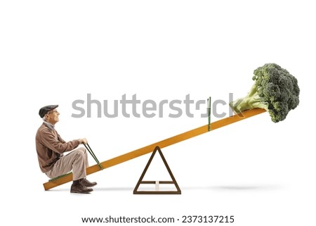 Full length profile shot of an elderly man and a broccoli on a seesaw isolated on white background