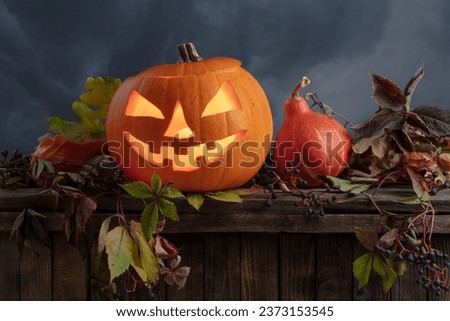 Halloween pumpkin head jack lantern with dried-up leaves. Halloween holidays art design. Carved Halloween pumpkin with burning candle on a background of cloudy sky.