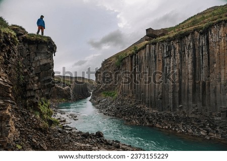 A discoverer is exploring the untouched nature in Iceland. A man is standing on a cliff in nature and watching the canyon river from the top. Royalty-Free Stock Photo #2373155229