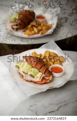 Croissant sandwich with fired potato, cheese, lettuce, tomatoes and sausage on the sofa. fresh sandwich on the table. Croissant Sandwich with fresh vegetables  Side and top view, close-up 