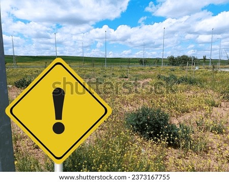 Electric field with signs with caution and exclamation marks, Aerial view of grass swaying on the field against the background of blue open sky landscape, electrical poles,