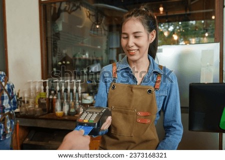 Young Asian business owner, cafe owner using card swiping machine charge customer counter smiling. Customers using credit cards pay bakery goods  coffee. single mother makes coffee orders in the back.