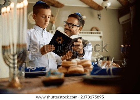 Jewish boy and his father reading Tanakh while celebrating Hanukkah at home. Royalty-Free Stock Photo #2373175895