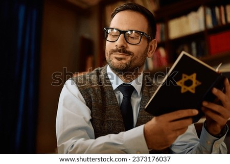 Mid adult Jewish man reading Tanakh at home.  Royalty-Free Stock Photo #2373176037