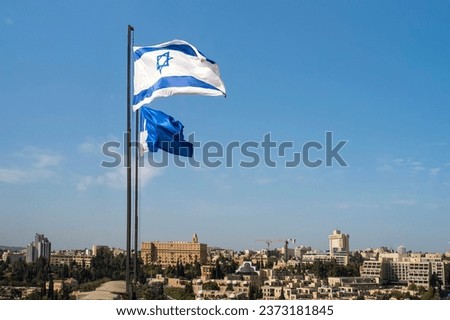 Israel and Jerusalem flags shot at blue cloudless sky background above the old city of Jerusalem Israel. Two flags flying against skyscape and cityscape. Recognized symbol of modern Jewish identity.