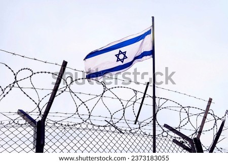 View of israeli flag behind barbed wire against cloudy sky. border post on the border of israel. The checkpoint at the embassy of the country. the Palestinian-Israeli border. Royalty-Free Stock Photo #2373183055