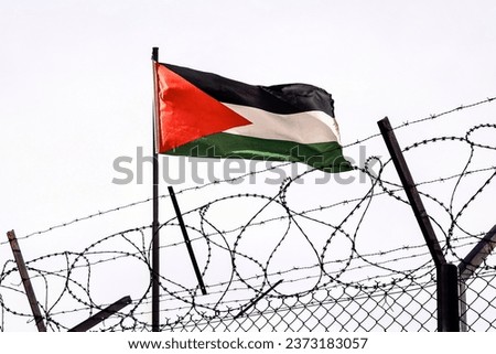 View of palestinian flag behind barbed wire against cloudy sky. border post on the border of palestine. The checkpoint at the embassy of the country. the Palestinian-Israeli border. Royalty-Free Stock Photo #2373183057