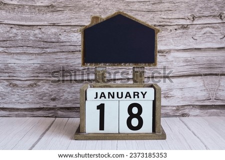 Chalkboard with January 18 calendar date on white cube block on wooden table.