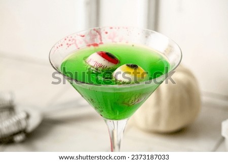 Glass of delicious green cocktail and eyes for Halloween celebration on light background, closeup