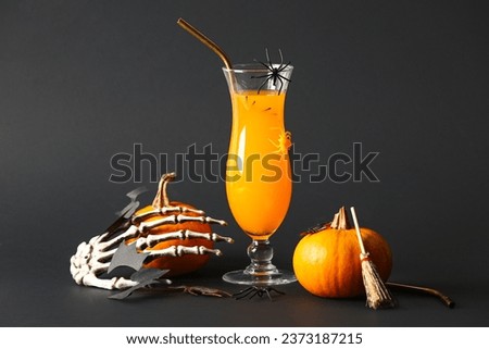 Glass of delicious orange cocktail, skeleton hand and pumpkins for Halloween celebration on black background
