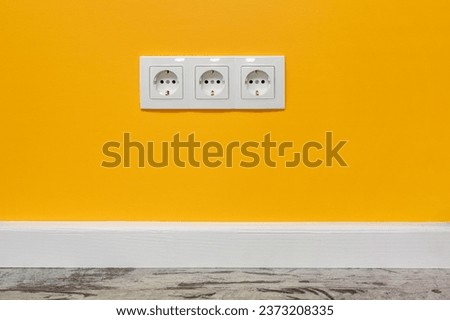 White triple outlet installed on the yellow wall, front view. Royalty-Free Stock Photo #2373208335