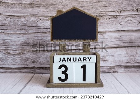 Chalkboard with January 31 calendar date on white cube block on wooden table.