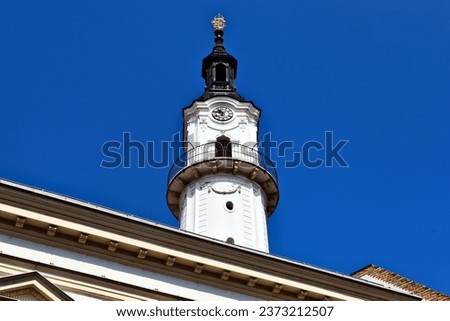 ornate white stucco fire-watch tower in the city of Veszprem, Hungary. low angle view. famous landmark. old architecture. travel and tourism concept. stucco house facade in the foreground. blue sky Royalty-Free Stock Photo #2373212507