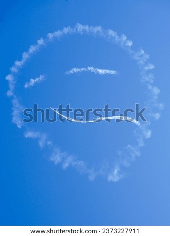 Smiley face shape in the blue sky created with aeroplane white smoke trails during aero show, face in the sky Royalty-Free Stock Photo #2373227911
